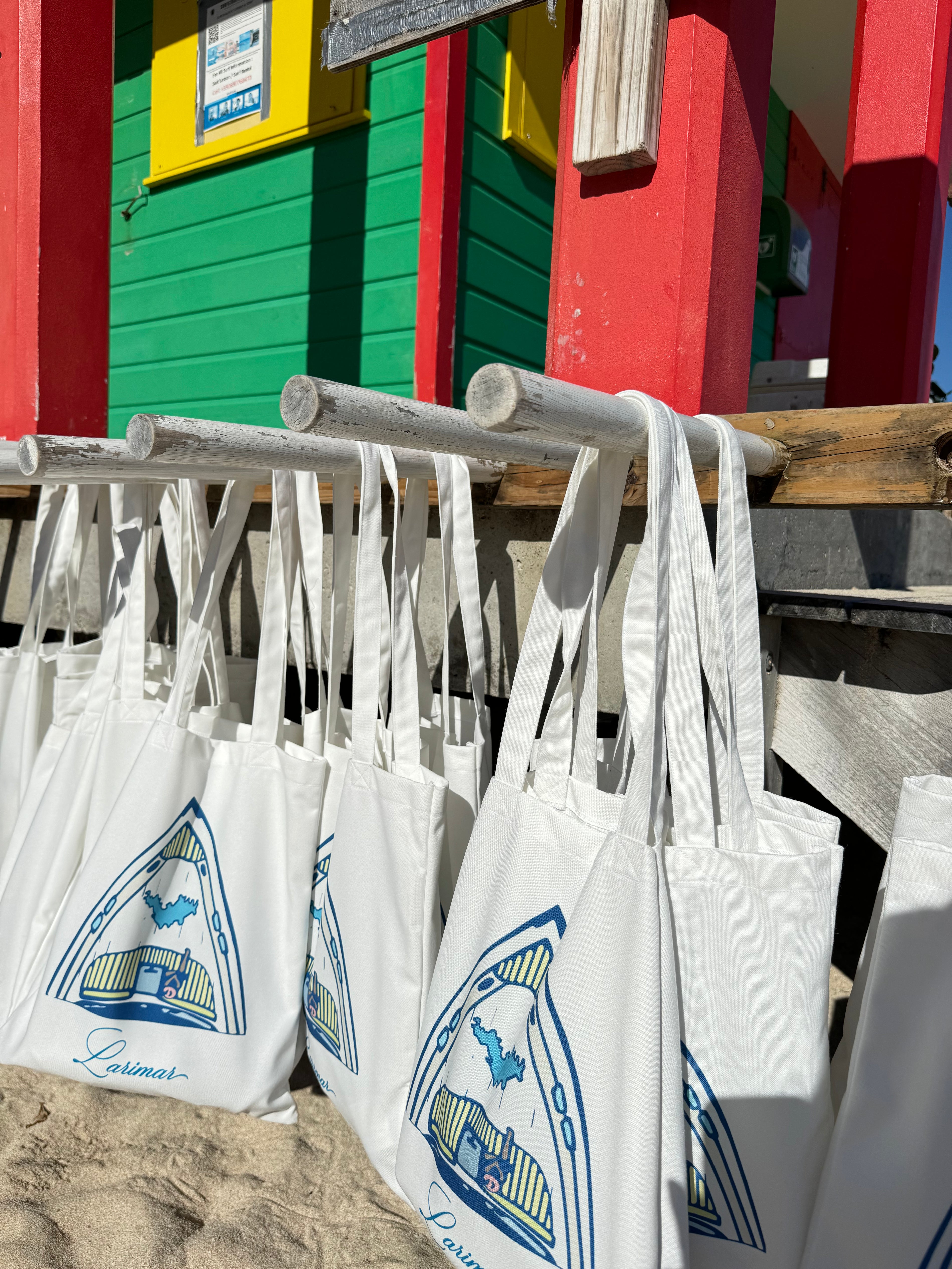 White tote bags with blue designs hanging on a wooden rack against a colorful background.